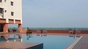 Piscina no terraço com vista clara do horizonte, cercada por um edifício com várias janelas e uma parede vermelha.