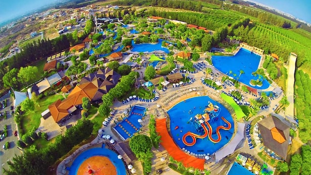 An aerial view of a resort with multiple swimming pools, a water slide, and a large circular pool with a central fountain. - Mediterranean dream with sea view and private pool  (Pissouri)