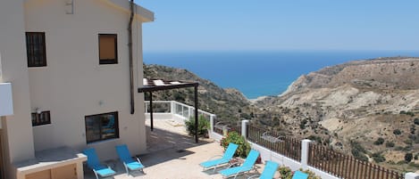 A pool area with lounge chairs and a view of the sea.
