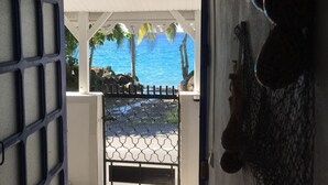 Uma entrada que dá para uma área externa coberta, com vista para o oceano e palmeiras.