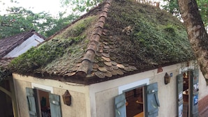Um edifício rústico com telhado coberto de musgo, base de tijolos e um pequeno alpendre.