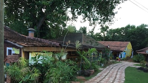 Uma vila rústica com casas tradicionais, um caminho de pedras e vegetação exuberante.