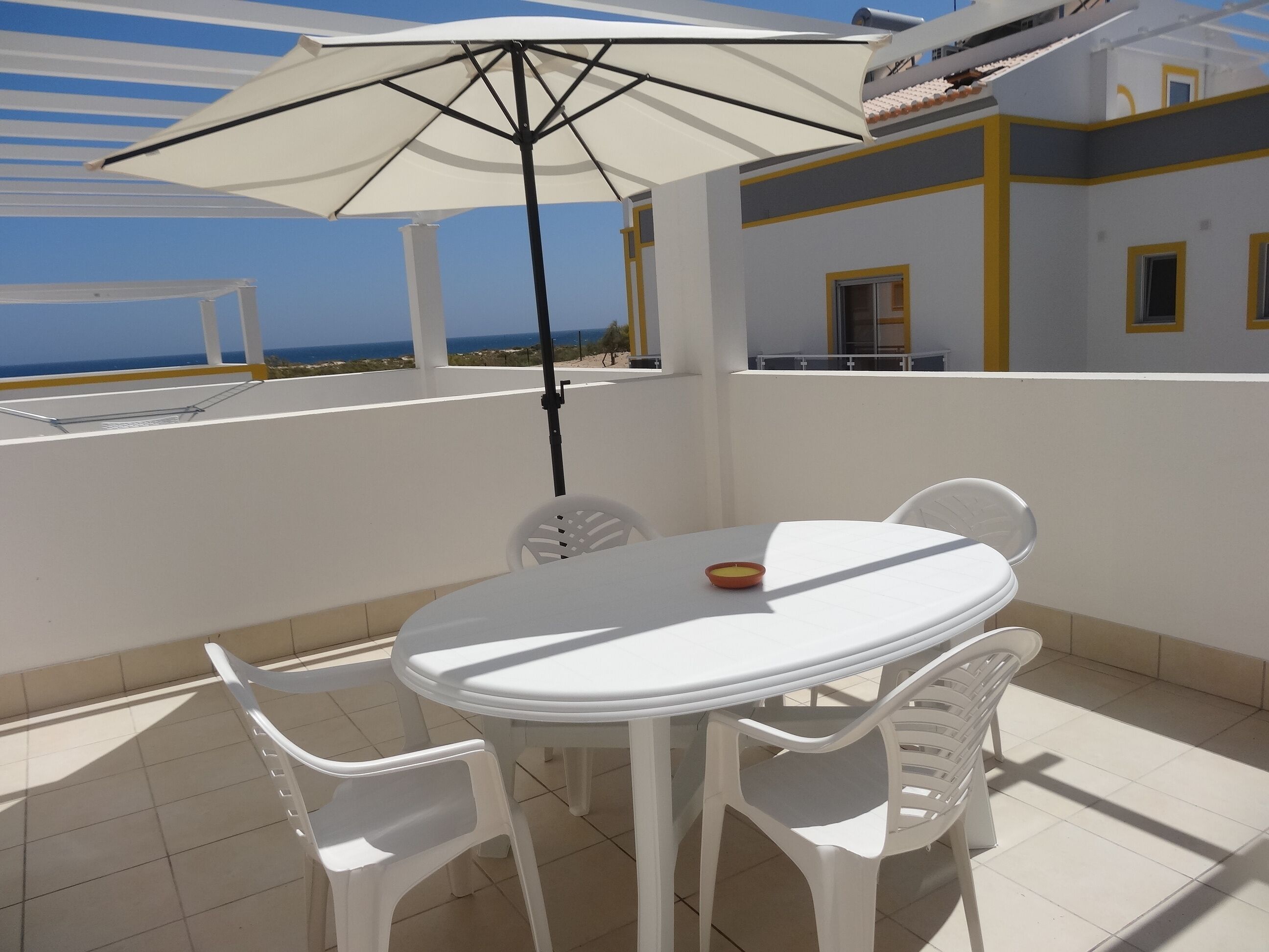 Una terraza con una mesa y sillas blancas, una sombrilla blanca y vista al mar.