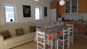 A modern kitchen with white cabinets, a dining table with chairs, and a sofa in the living area. - New 3-bedroom apartment 50 meters from the beach (Vila Real de Santo António)