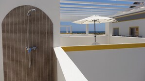 A modern outdoor area with a tiled wall, a white umbrella, and a view of the sea. - New 3-bedroom apartment 50 meters from the beach (Vila Real de Santo António)