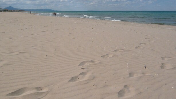 Une vaste plage de sable, parsemée d’empreintes, et un ciel dégagé.
