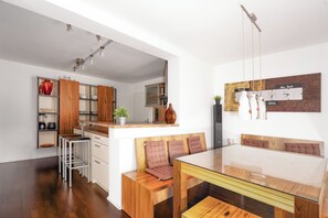 A modern kitchen with wooden cabinets, a built-in stove, and a dining area with a glass table and wooden bench.
