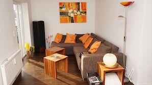 Ein modernes Wohnzimmer mit einem Ecksofa, einem Holztisch, einer Stehlampe und einem Bild an der Wand.