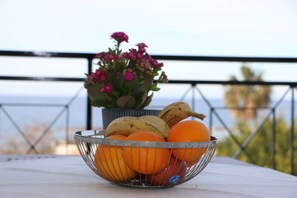 Ein Obstkorb aus Metall auf einem Tisch mit Bananen, Orangen und Äpfeln.