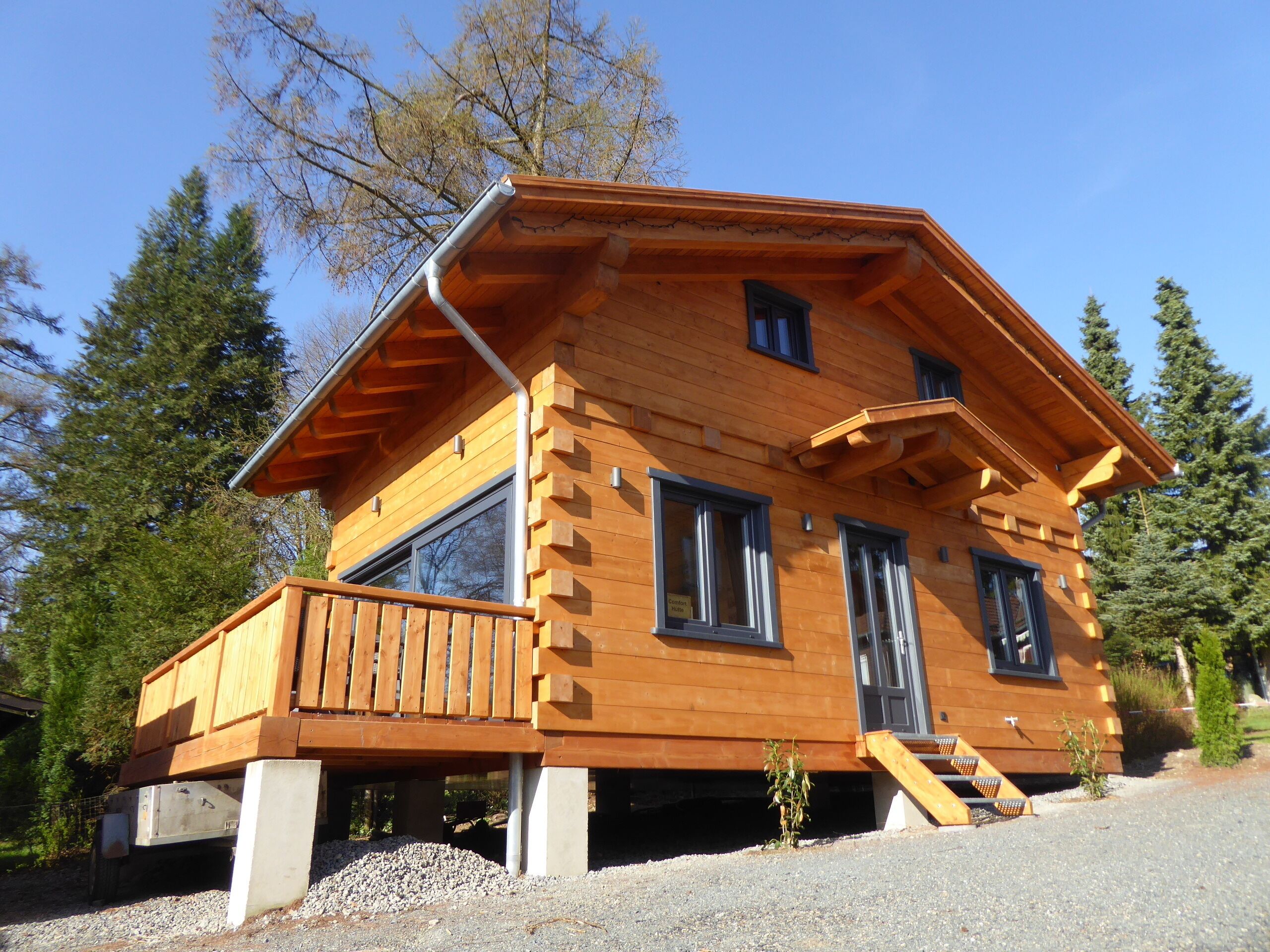 A wooden cabin with a balcony, large windows, and a small porch.