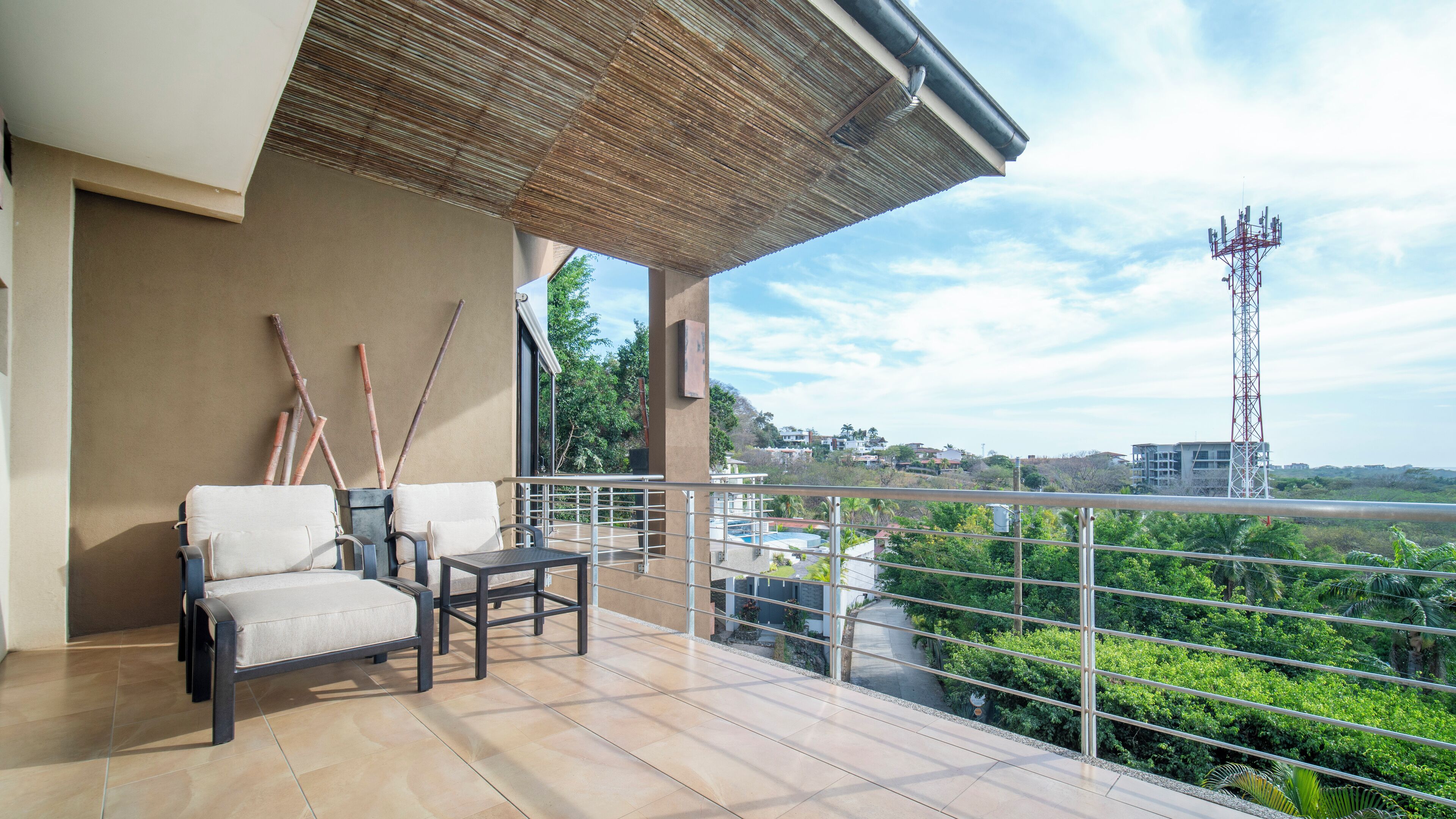 Un balcón con dos sillas y una mesa, con vistas a una piscina y follaje.