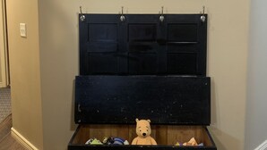 Una habitación con un cuadro grande de un atardecer sobre el océano, un mueble negro para guardar objetos con un osito de peluche, y suelo de madera.
