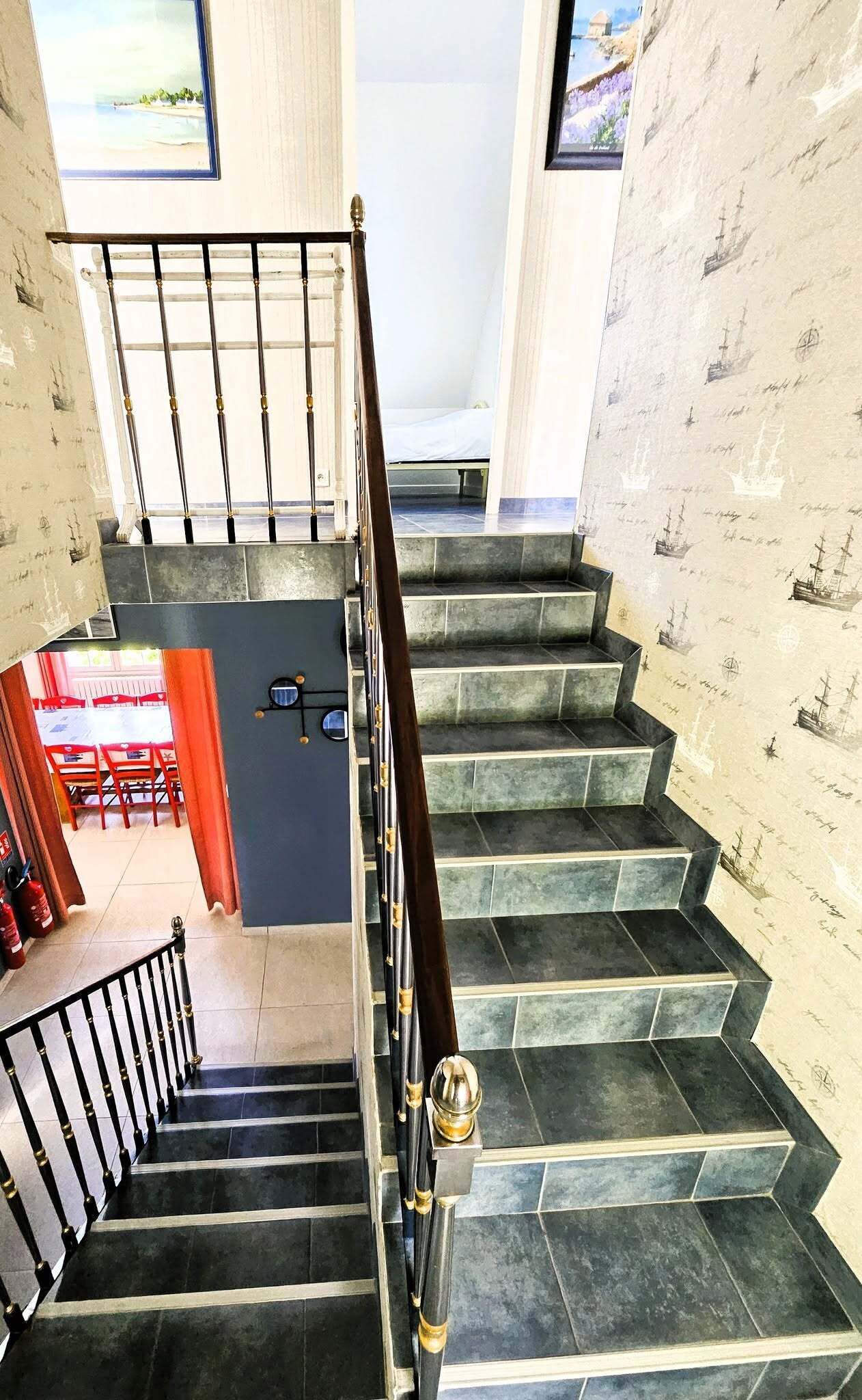 Una escalera con barandilla de madera oscura y balaustres negros que conduce a una habitación con cama y ventana con vista a una playa.