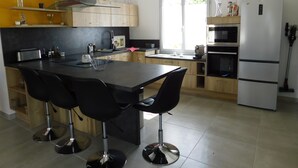 A modern kitchen with a central island, bar stools, a refrigerator, and a microwave. - The oustaou of Sandrine (Valréas)