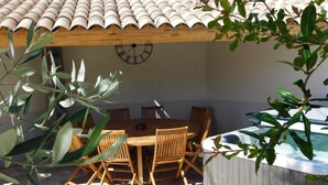 An outdoor patio with a wooden table and chairs, a clock on the wall, and a hot tub. - The oustaou of Sandrine (Valréas)
