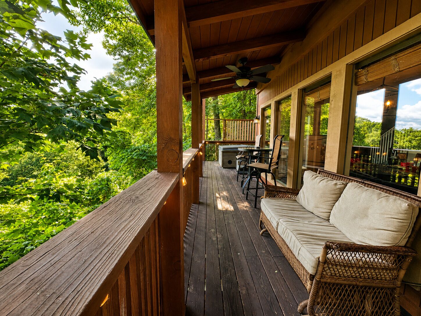 Eine Holzterrasse mit einer Couch und Sesseln, einem Tisch mit Stühlen sowie einem Deckenventilator.