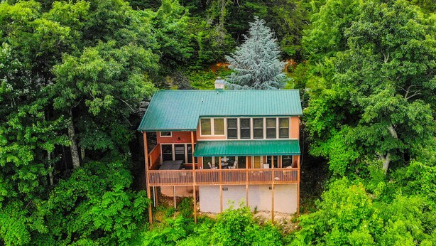 Eine zweistöckige Hütte mit einem grünen Dach, umgeben von dichtem Wald.