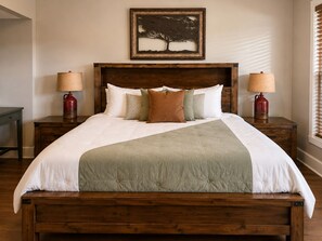A neatly made bed with a wooden headboard, two bedside lamps, and a framed artwork above.