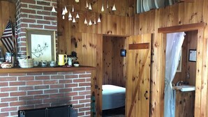 Ein rustikales Blockhaus mit Kamin aus Ziegelsteinen, Holzwänden, einem Bett und einem Badezimmer mit Dusche.