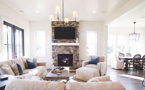 A spacious living room with a stone fireplace, a flat-screen TV, and a dining area with a table and chairs.