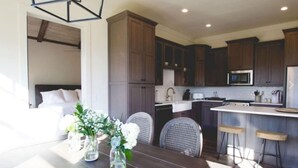 A modern kitchen with dark wooden cabinets, a central island with stools, and a dining area with a table and chairs. - Luxury Farmhouse Cottage on Winery (Dahlonega)