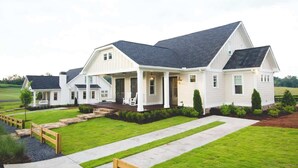 A two-story house with a covered porch, a well-maintained lawn, and a stone pathway leading to the entrance. - Luxury Farmhouse Cottage on Winery (Dahlonega)