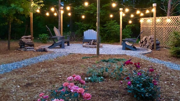 Een tuin met een grindpad, houten stoelen en lichtjes.