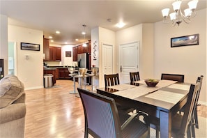 A modern kitchen with wooden cabinets, a refrigerator, and a dining area with a black table and chairs. - THE HIGHTOWER SUITE- A Luxury top floor Condo in the Center of Girdwood/Alyeska! (Girdwood)