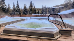 Un bain à remous doté d’une terrasse en bois, entouré d’arbres couverts de neige et surplombant un ciel dégagé.