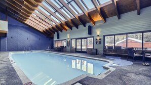 Une piscine intérieure avec un plafond en bois, de grandes fenêtres et un panneau indiquant « Aucun sauveteur de service ».