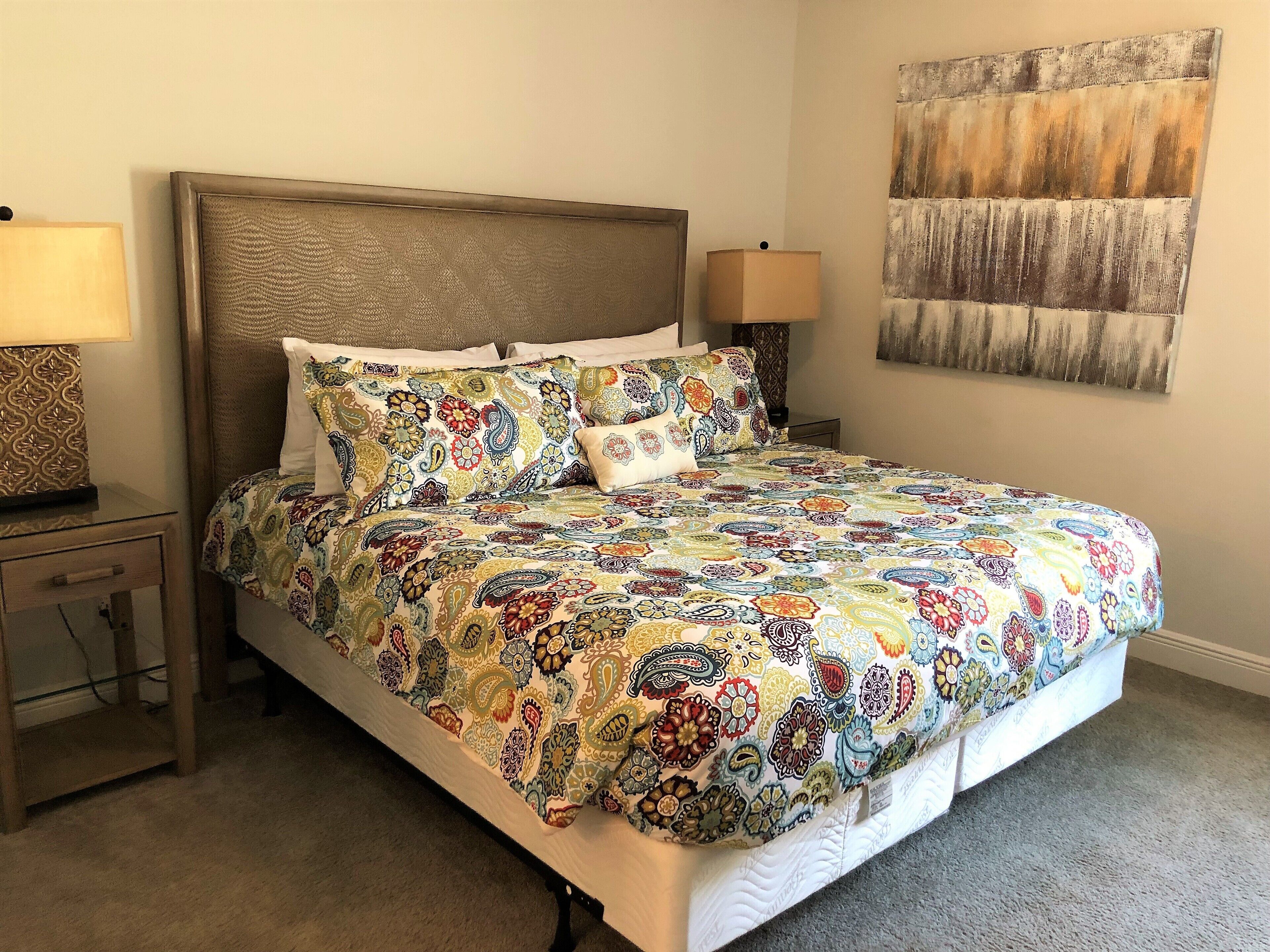A bed with a colorful patterned bedspread, two bedside tables with lamps, and a large abstract painting on the wall.