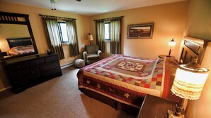 A bedroom with a large bed, a dresser, a chair, a lamp, and a window with curtains. - Rockin Y, Romantic Getaway or Family Friendly Lodging (Gardiner)