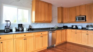 A modern kitchen with wooden cabinets, a built-in microwave, and a dishwasher. - Spacious 4-Bedroom Home near Lagoon, Beach & Hatley Castle (Victoria)