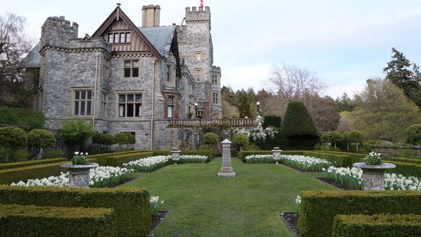 A large stone castle with a symmetrical garden, featuring manicured hedges and white flowers. - Spacious 4-Bedroom Home near Lagoon, Beach & Hatley Castle (Victoria)