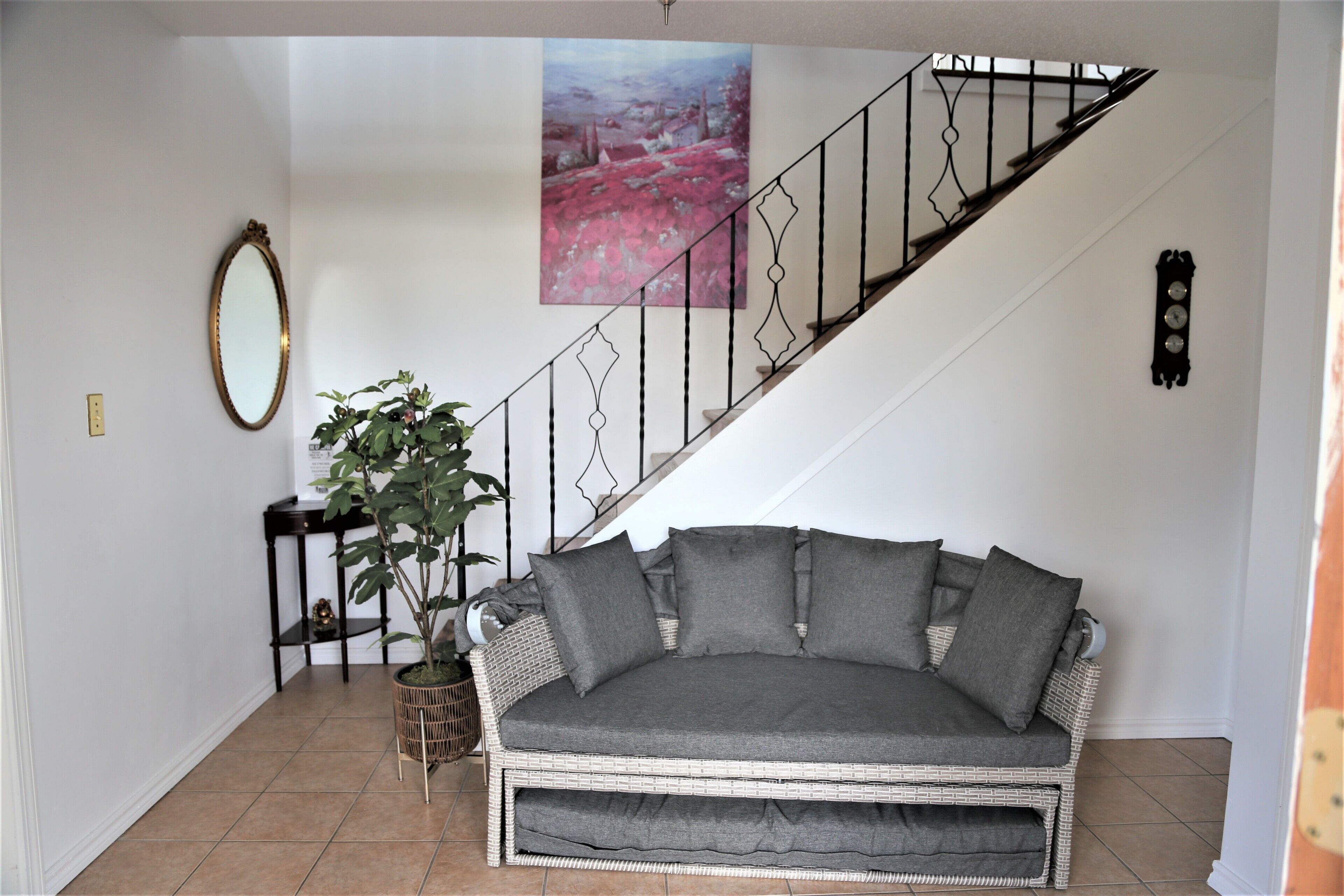 Un salon avec un canapé en osier, une plante en pot, un tableau et un escalier.