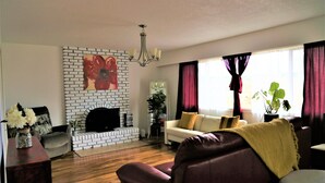 A living room with a fireplace, a sofa, a coffee table, and a TV. - Spacious 4-Bedroom Home near Lagoon, Beach & Hatley Castle (Victoria)