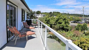 A balcony with outdoor furniture, a glass railing, and a view of a residential area with houses and greenery. - Spacious 4-Bedroom Home near Lagoon, Beach & Hatley Castle (Victoria)