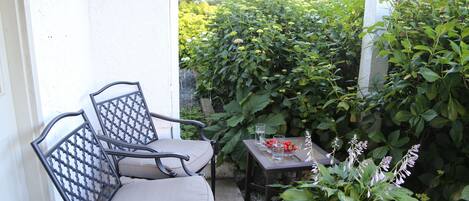 An outdoor seating area with two chairs and a table, surrounded by lush greenery.