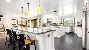 A spacious kitchen with white cabinetry, a large island with bar stools, and pendant lighting. - Wine Country Estate with Vineyard Views, Pool, Spa, Fire-pit, 4 bedroom Suites (Temecula)