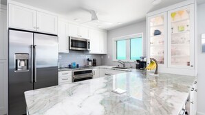 A modern kitchen with white cabinets, stainless steel appliances, a marble countertop, and a large window. - Ultimate Sanibel Beachfront! Island Beach Club, Top Floor, West-Facing, End Unit (Sanibel)