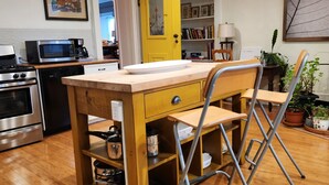 A compact kitchen with a wooden table and chairs, a yellow door, and a bookshelf with books and decorative items. - Curricle The third of the houses of the stone chariot (Prince Edward)