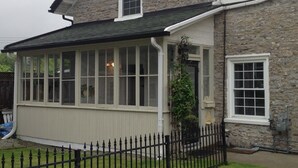 A two-story stone house with a covered porch and a black metal fence. - Curricle The third of the houses of the stone chariot (Prince Edward)