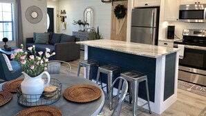 A modern kitchen with stainless steel appliances, a central island with stools, and a dining area with a round table and wicker placemats. - The Casa Coco | Garden : Modern and relaxing home  with heated pool  (Venice)