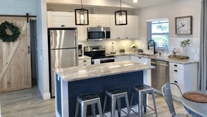 A modern kitchen with stainless steel appliances, a central island with stools, pendant lighting, and a view to the outside. - The Casa Coco | Garden : Modern and relaxing home  with heated pool  (Venice)