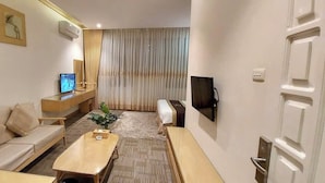 Une chambre d’hôtel moderne, dotée d’un canapé, d’une table basse en bois, d’une télévision et d’une grande fenêtre avec des rideaux.
