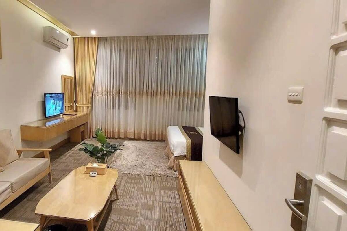 Une chambre d’hôtel moderne, dotée d’un canapé, d’une table basse en bois, d’une télévision et d’une grande fenêtre avec des rideaux.