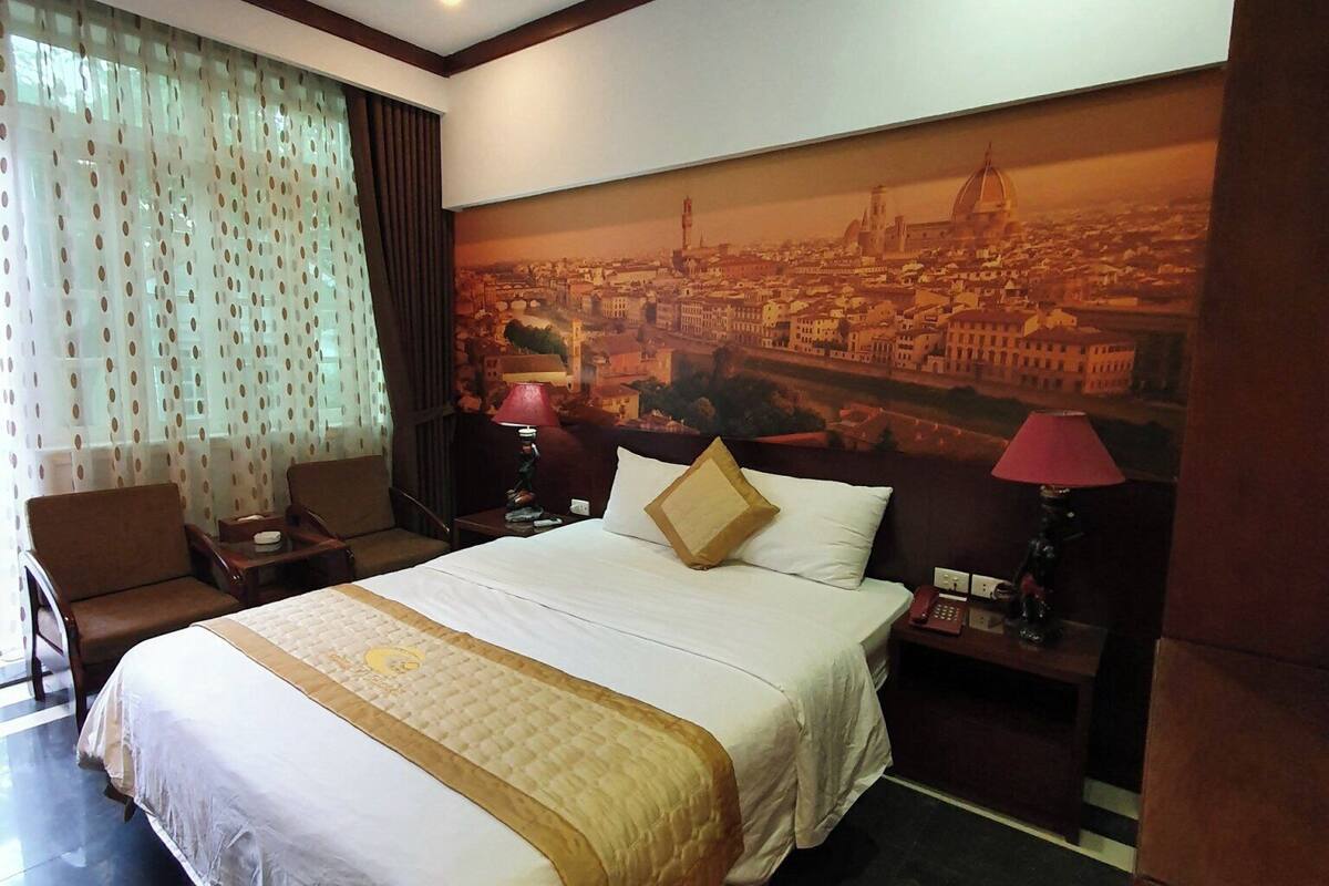 Une chambre d’hôtel avec un grand lit, un canapé, un bureau et un tableau représentant un paysage urbain accroché au mur.