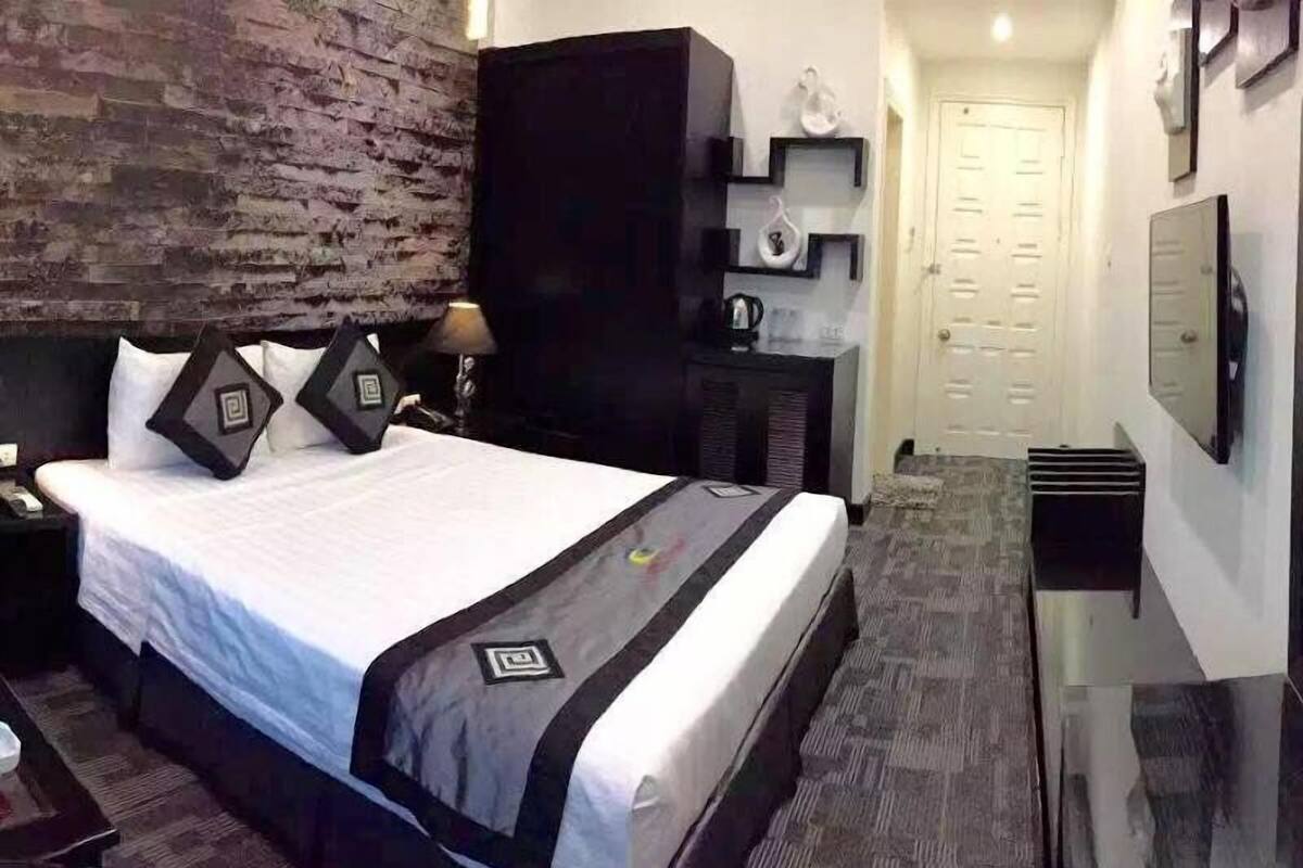 Une chambre d’hôtel avec un grand lit, une armoire sombre, un petit bureau et un miroir au mur.