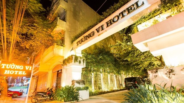 L’extérieur de l’hôtel Tuong Vi, avec son panneau indicateur, une moto garée devant et une entrée bien éclairée.