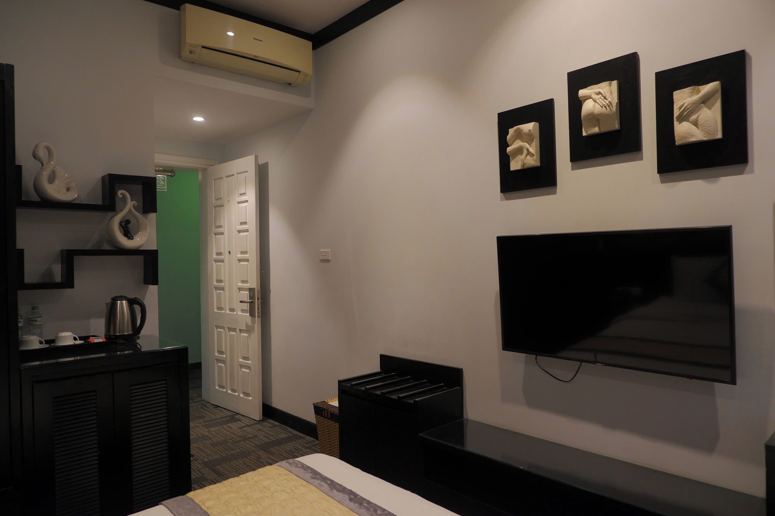 A modern hotel room with a flat-screen TV, a bed, a coffee maker, and a small trash bin.